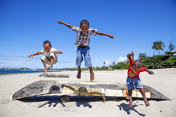 drie jongens springen op een strand over een bootje